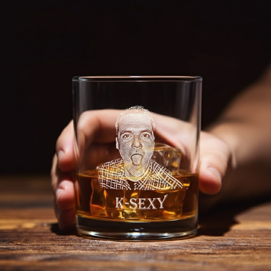 Whiskey glass held in hand, filled with amber liquid, featuring laser-engraved portrait of man with tongue out and text "K-SEXY" below