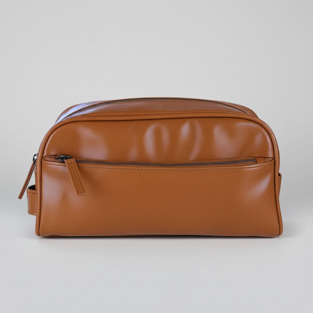 Tan leather toiletry bag with front zipper pocket and carrying handle, displayed against neutral background