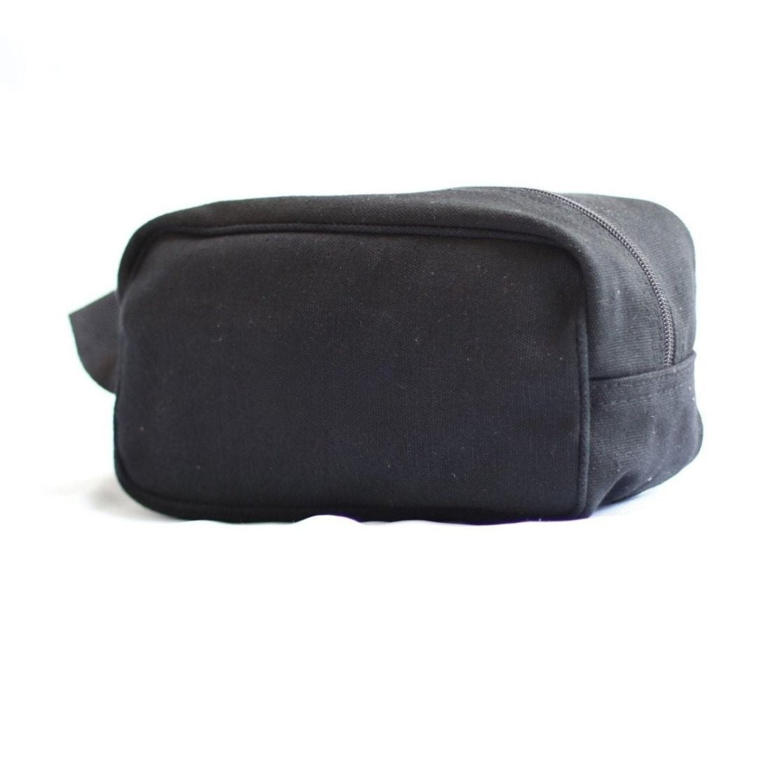 Black canvas toiletry bag with rectangular shape, flat base, and top zipper closure shown from angled side view