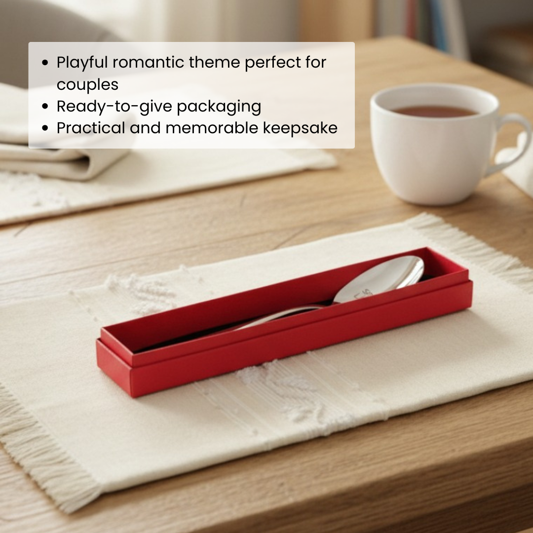 Red gift box containing stainless steel fork and spoon with engraved romantic phrases, displayed on white cloth with coffee mug in background