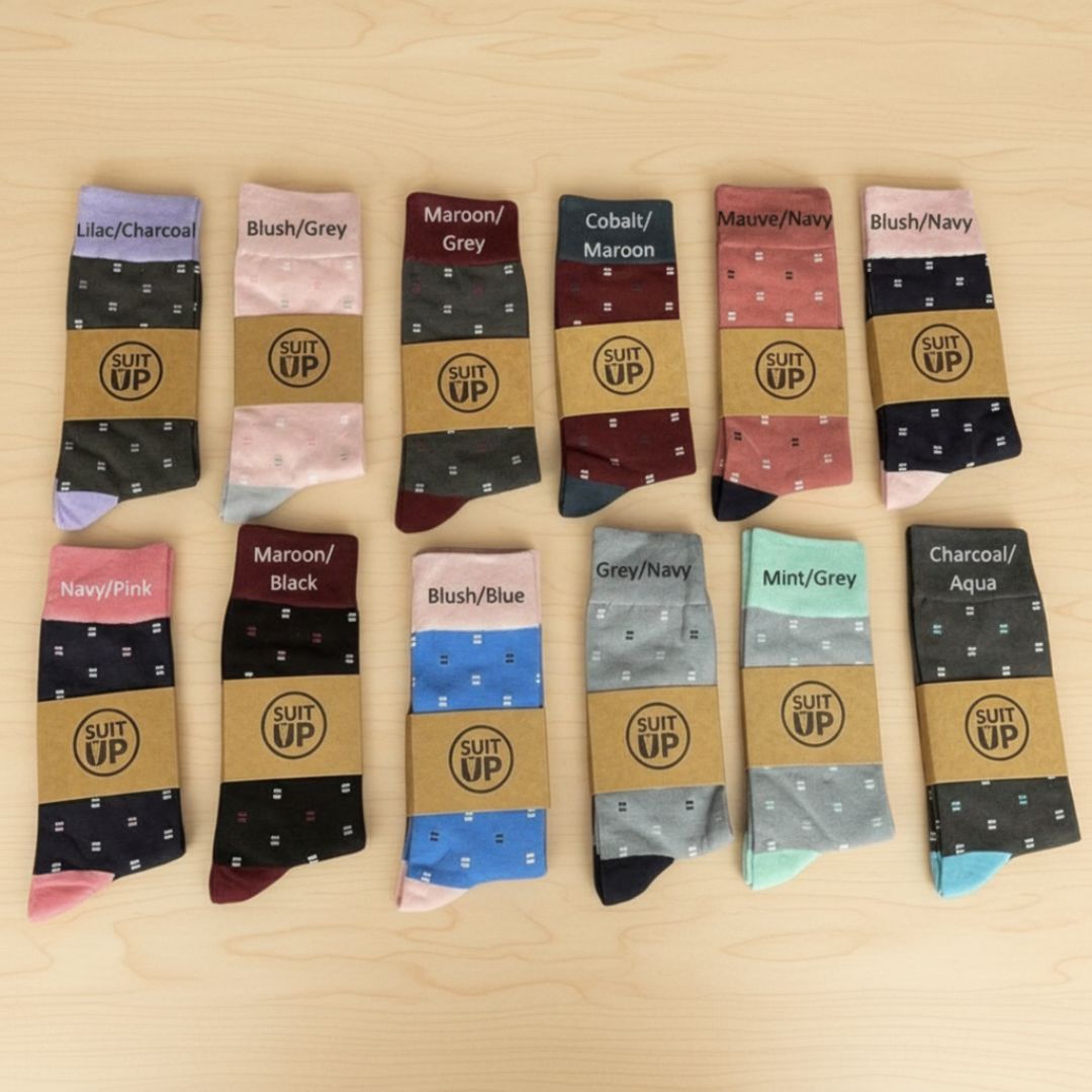 Grid layout displaying twelve color and pattern options for dress socks, each pair featuring the "Suit Up" logo and small geometric print details in various color combinations including lilac, blush, maroon, cobalt, mint, and charcoal.