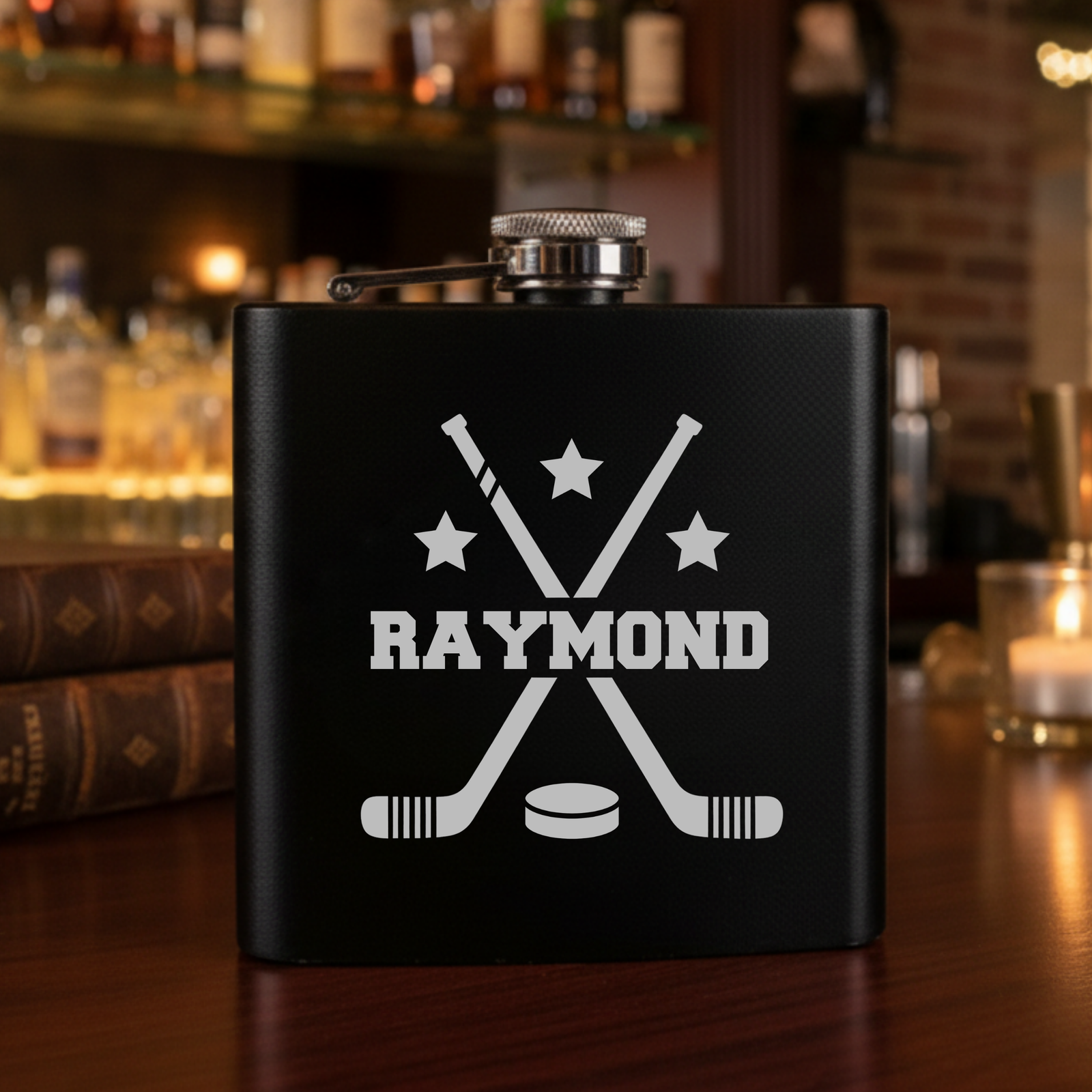 Black matte flask with laser-etched hockey design featuring crossed sticks, puck, stars, and personalized name "RAYMOND" in white lettering