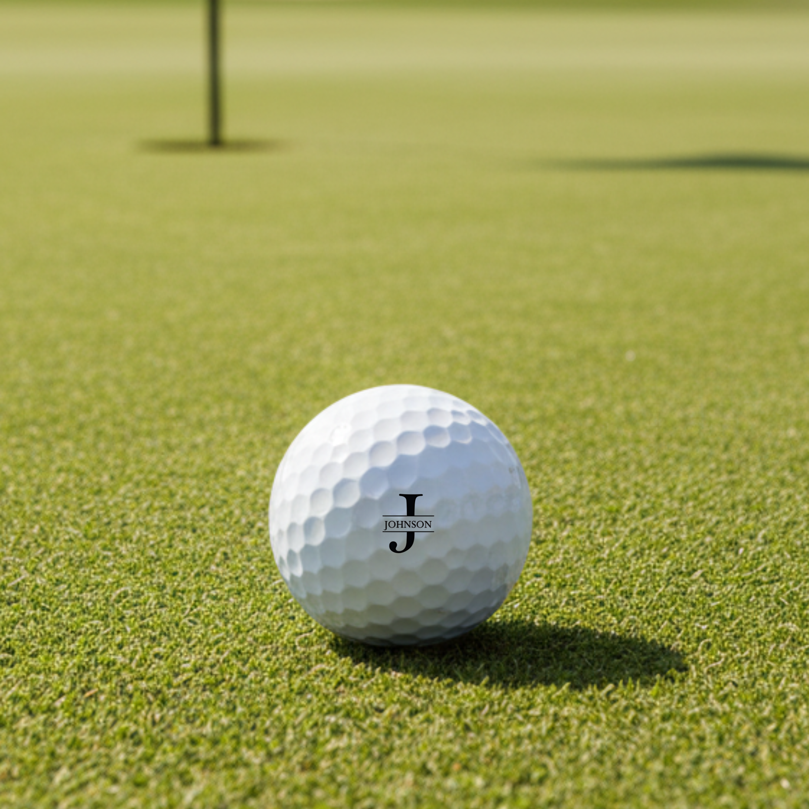 White golf ball with personalized sample engraving reading "JOHNSON" with decorative monogram on putting green with flagstick in background