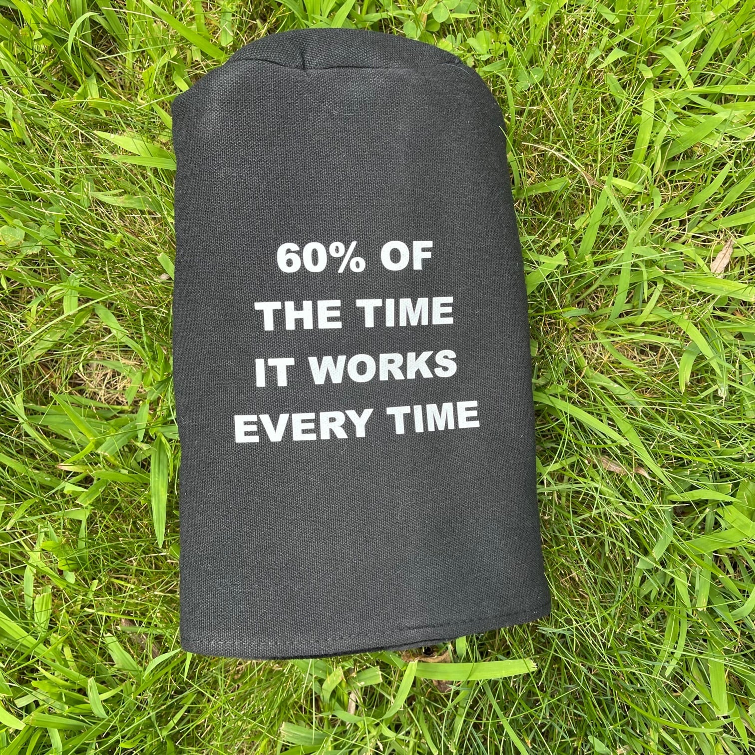 Charcoal koozie with white printed text reading "60% of the time it works every time" displayed on grass background