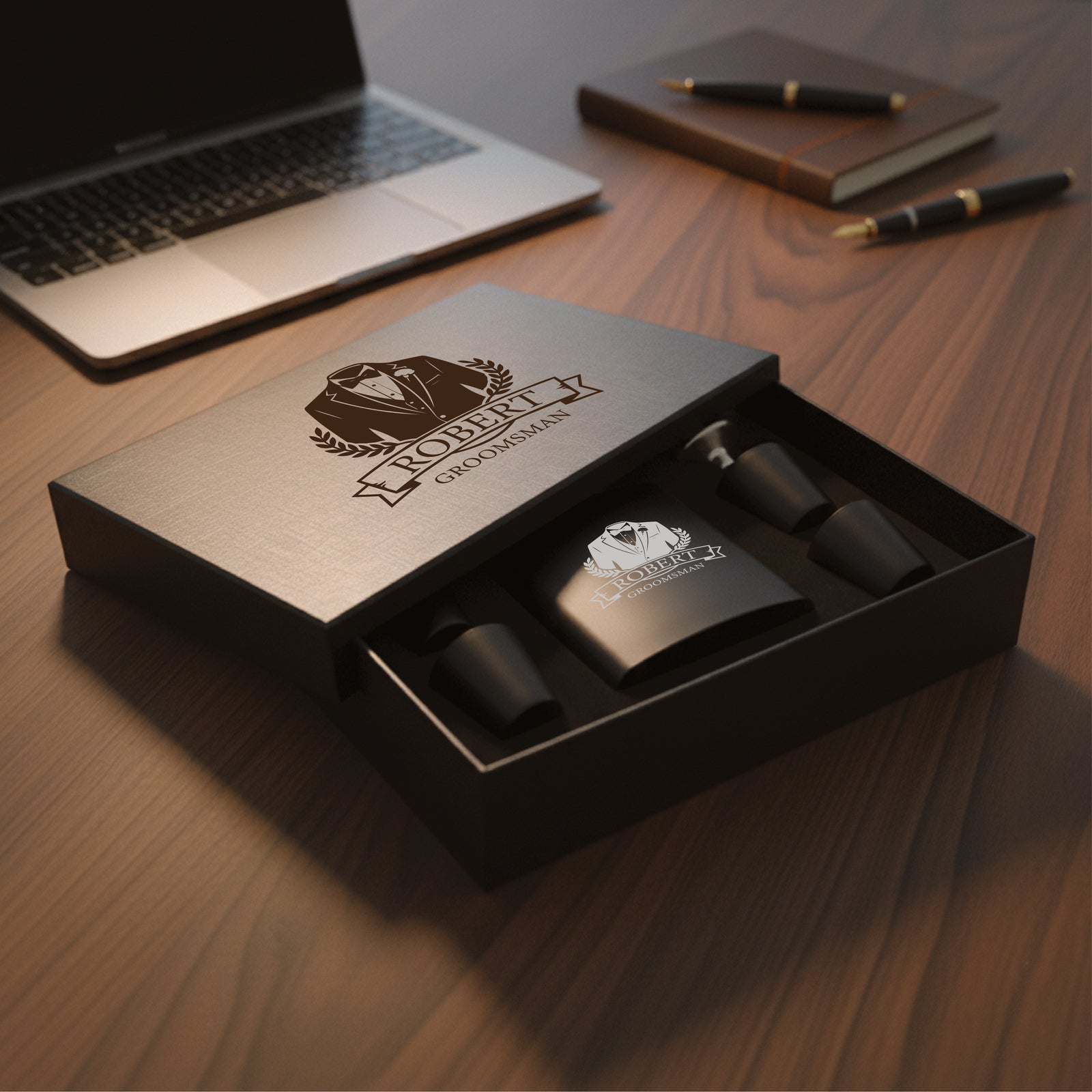 Gift set box open showing personalized flask engraved with sample design "Robert Groomsman" and matching black shot glasses inside kraft packaging