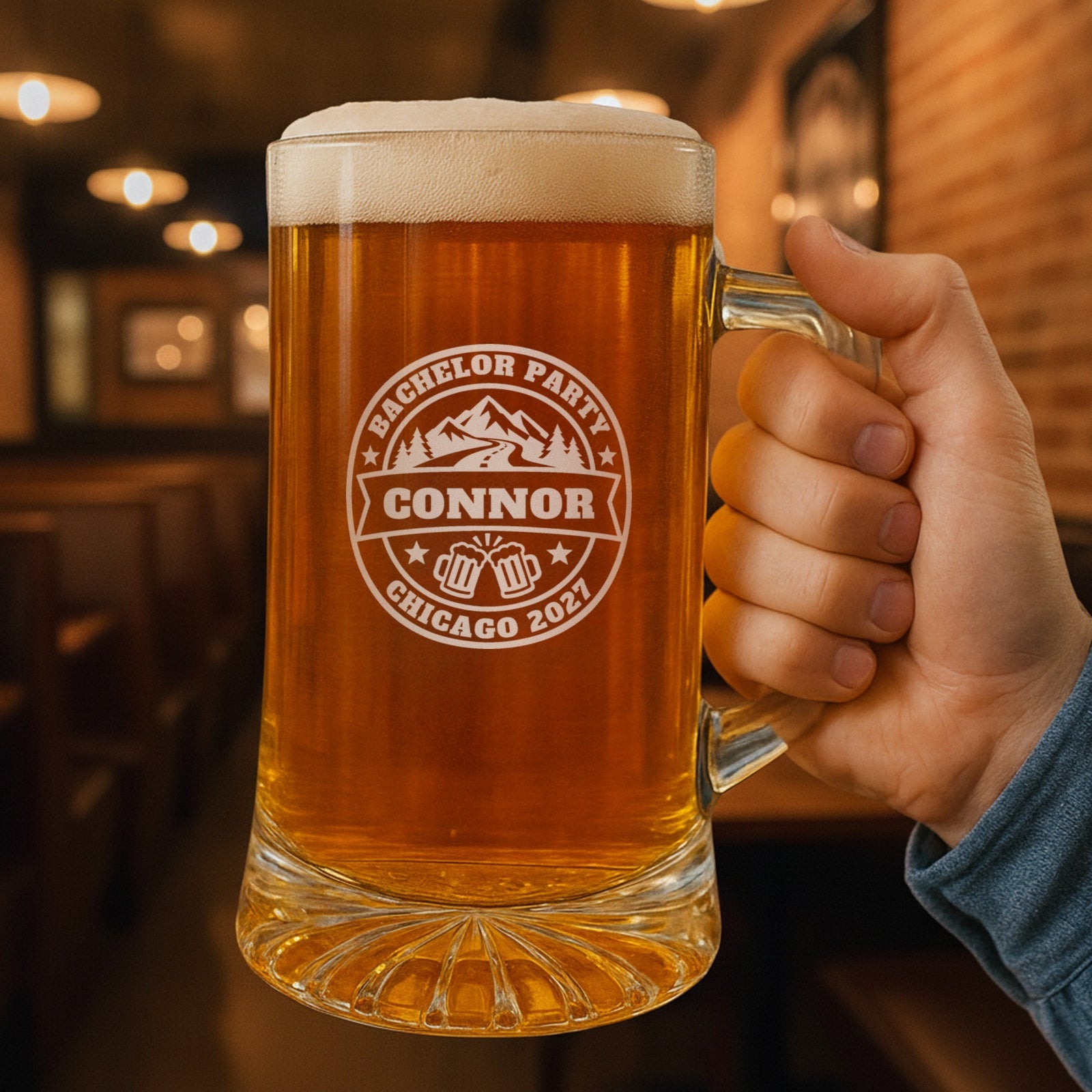 Hand holding a 25 oz personalized bachelor party beer stein in a pub, engraved with the mountain road badge, Bachelor Party, Connor and Chicago 2027