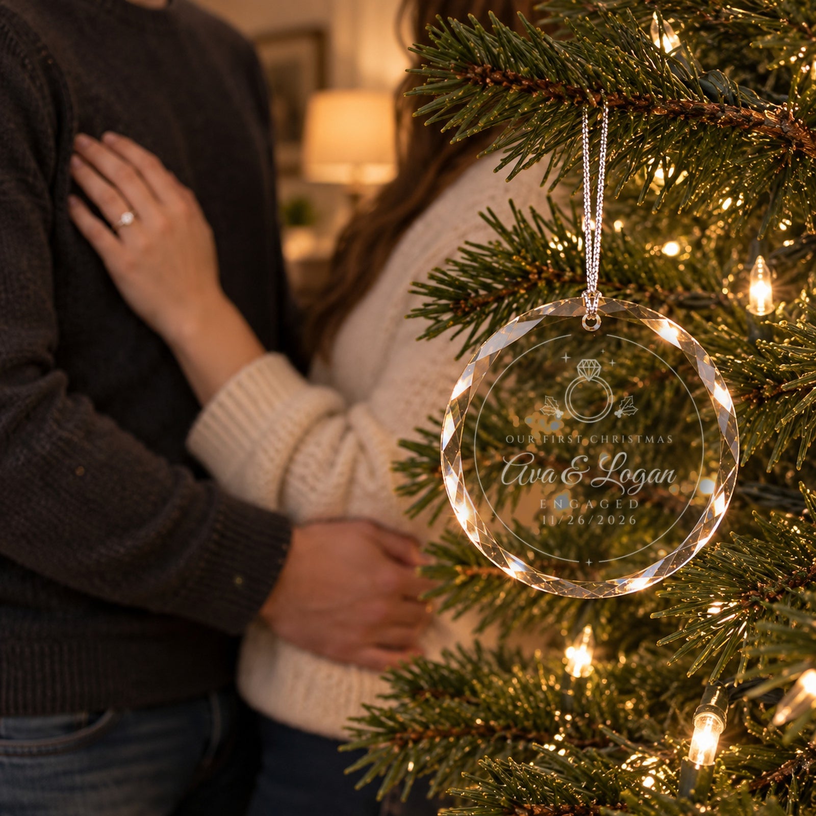 Newly engaged couple by their Christmas tree with the engraved engagement ornament hanging in front, reading Ava & Logan, ENGAGED 11/26/2026