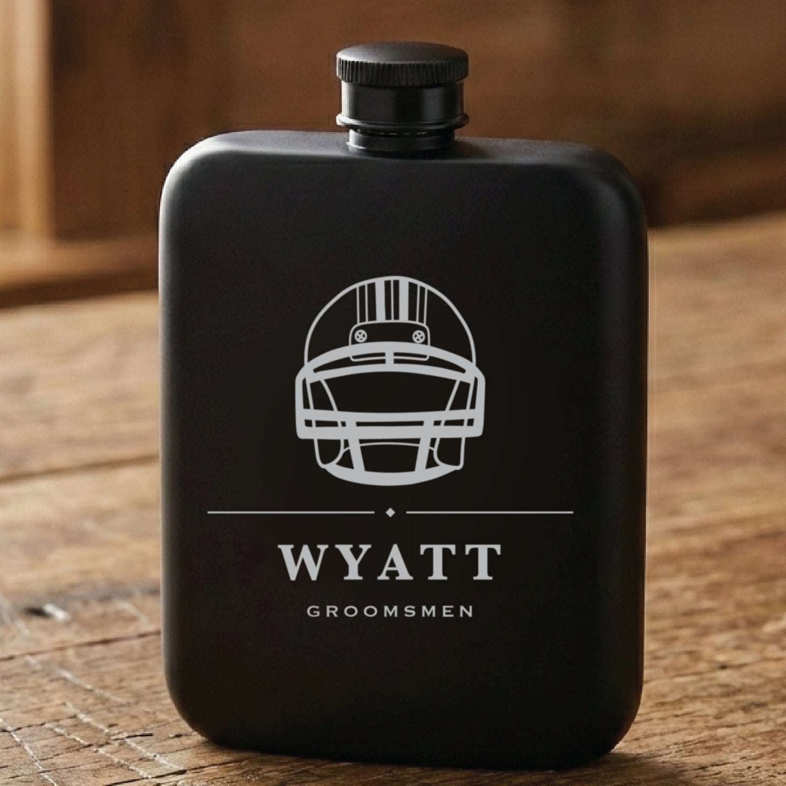 Matte black football groomsmen flask laser engraved with a football, the name Wyatt and the word Groomsmen beneath it.