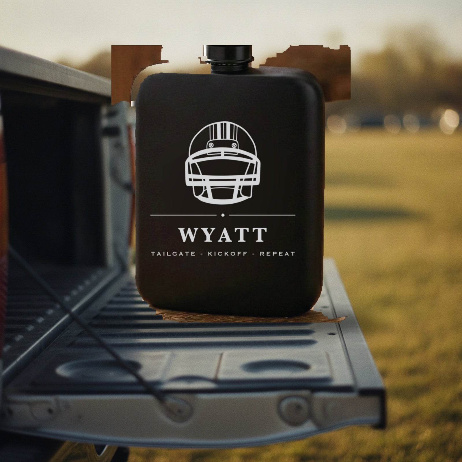 Personalized football flask engraved Tailgate Kickoff Repeat standing on the steel tailgate of a pickup truck on an autumn afternoon.