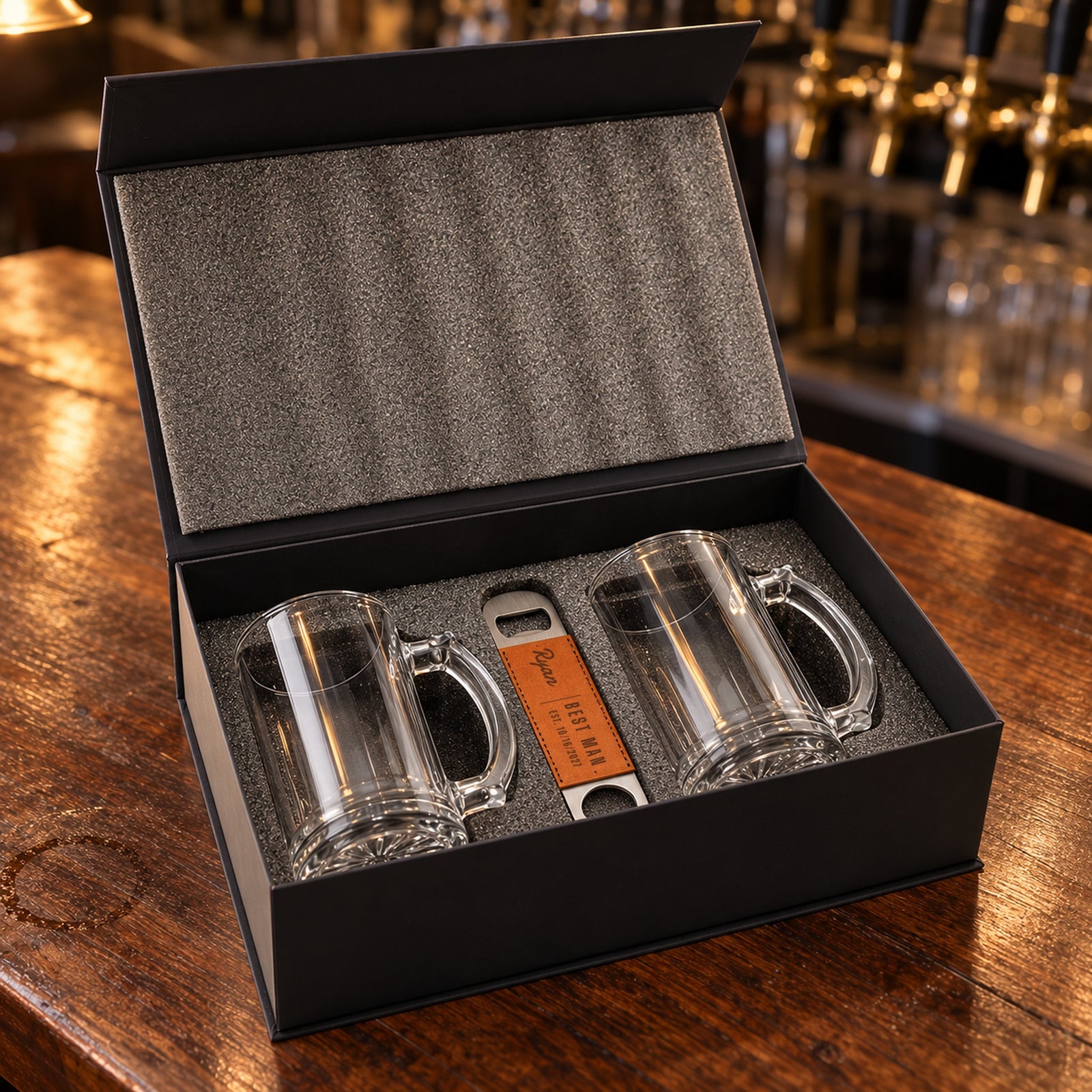 Groomsmen beer set open in its foam-lined gift box: two glass beer mugs and a bottle opener engraved Ryan, Best Man, Est. 10/16/2027