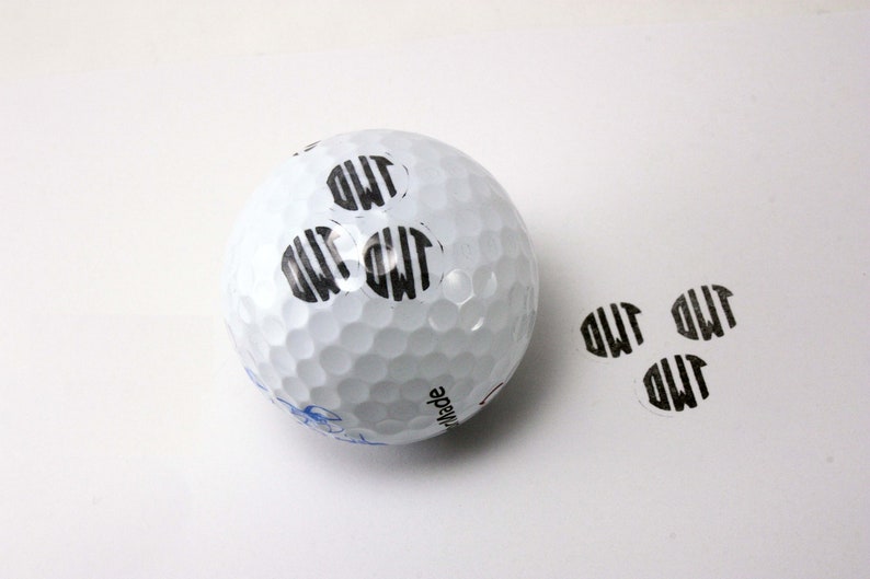 White golf ball with sample "GWF" monogram stamp impressions shown on ball surface and separately below