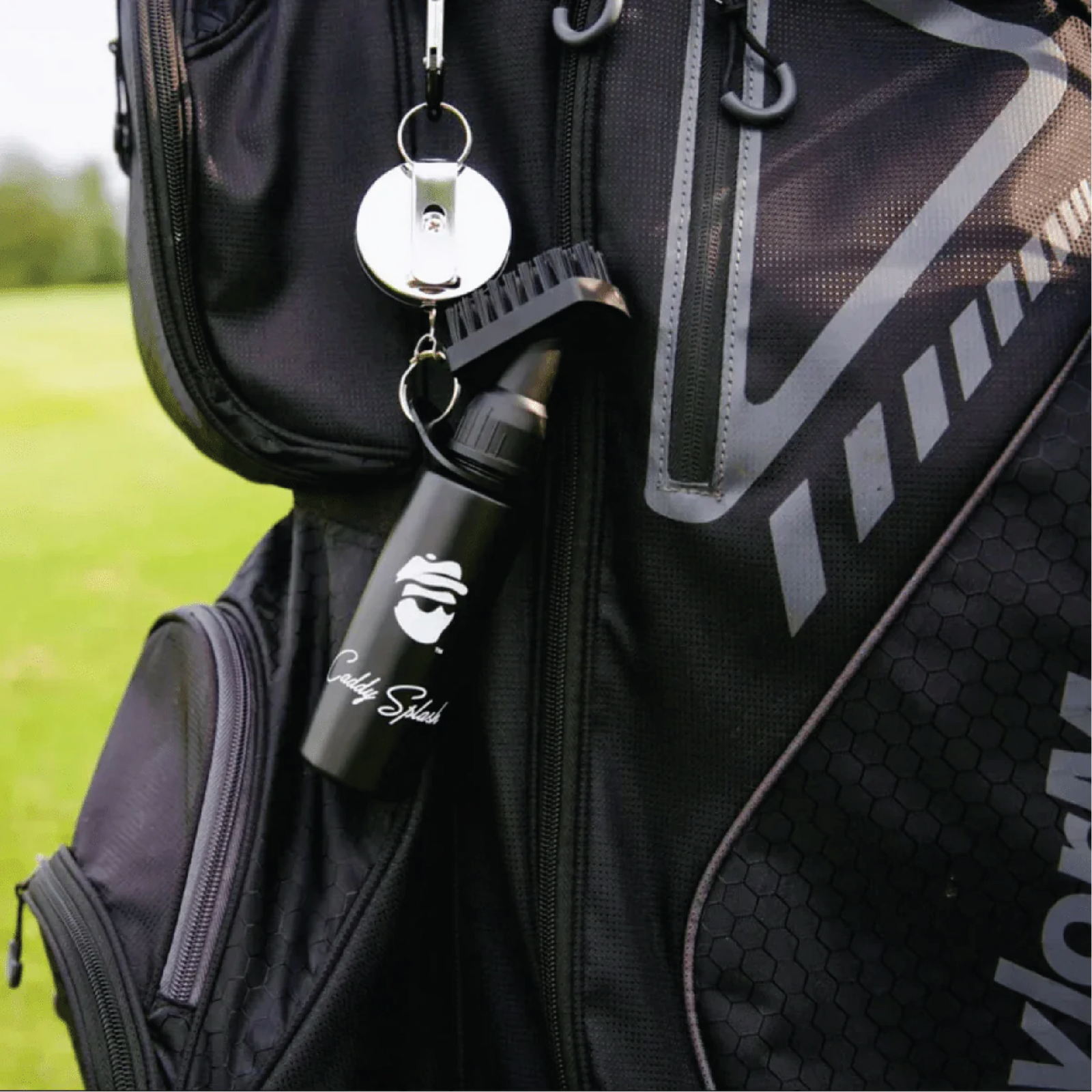 Black golf bag with personalized water bottle hanging from clip, showing engraved sample text, paired with metal reel keychain attachment.