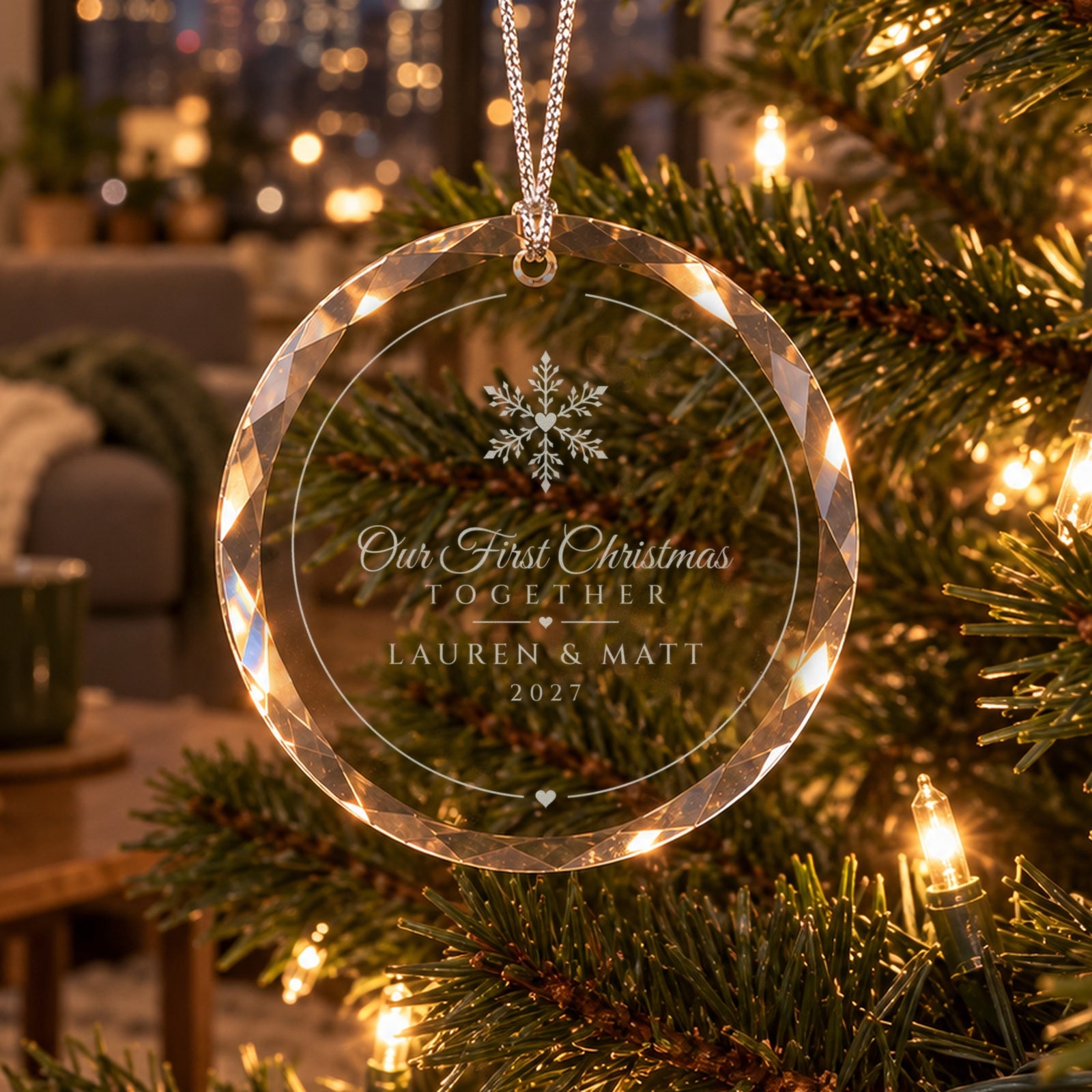 Classic Snowflake Our First Christmas Together ornament hanging on a lit tree in a cozy living room, engraved LAUREN & MATT, 2027