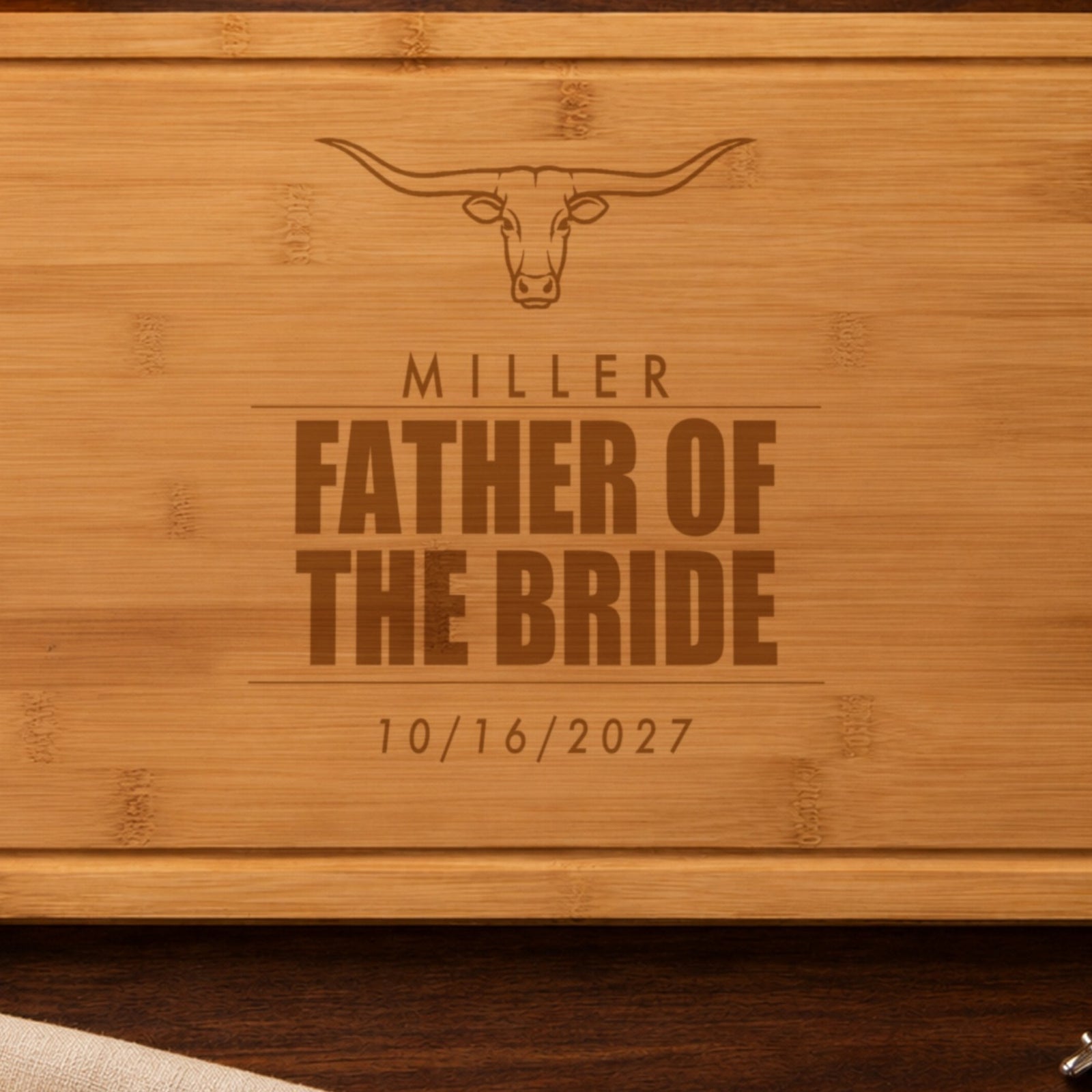 Close-up of the laser engraving on the father of the bride cutting board: the longhorn steer, MILLER and FATHER OF THE BRIDE burned into the bamboo