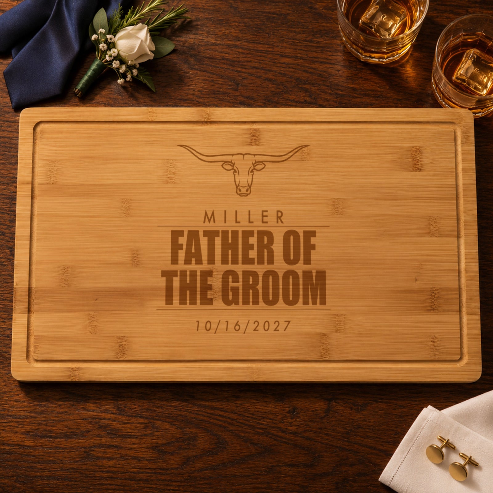 Personalized father of the groom cutting board engraved with a longhorn, MILLER, FATHER OF THE GROOM and 10/16/2027 at a rehearsal dinner with whiskey and a navy tie