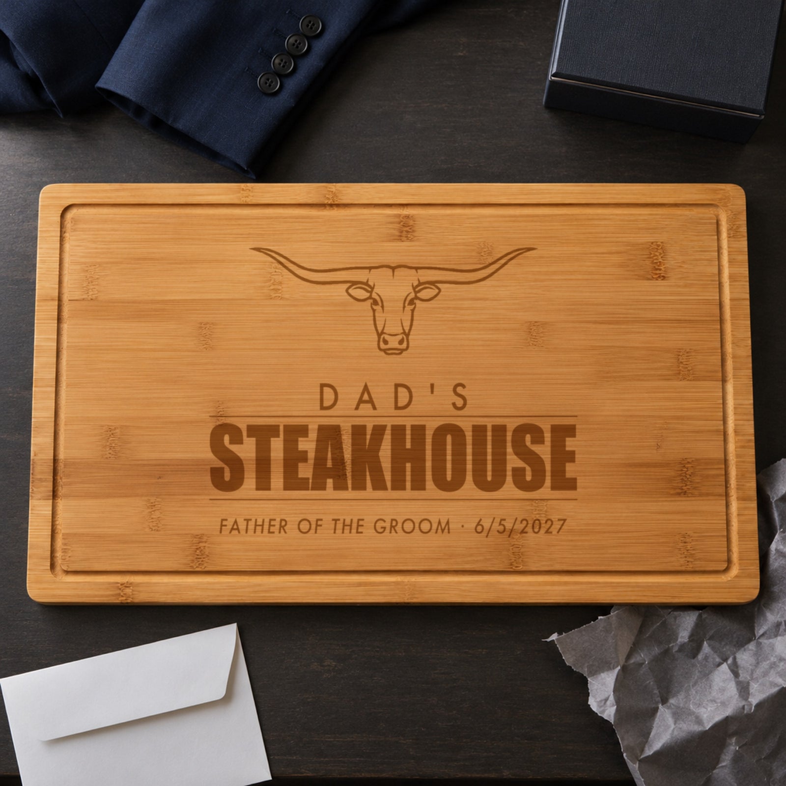 Father of the groom gift from the groom: a steakhouse cutting board engraved DAD'S STEAKHOUSE, FATHER OF THE GROOM 6/5/2027, unwrapped on the wedding morning