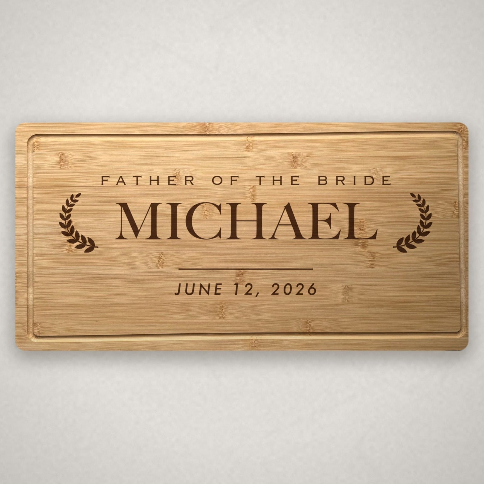 Personalized wedding party cutting board in solid bamboo, engraved Father of the Bride above the name Michael between two laurel branches with the wedding date below.