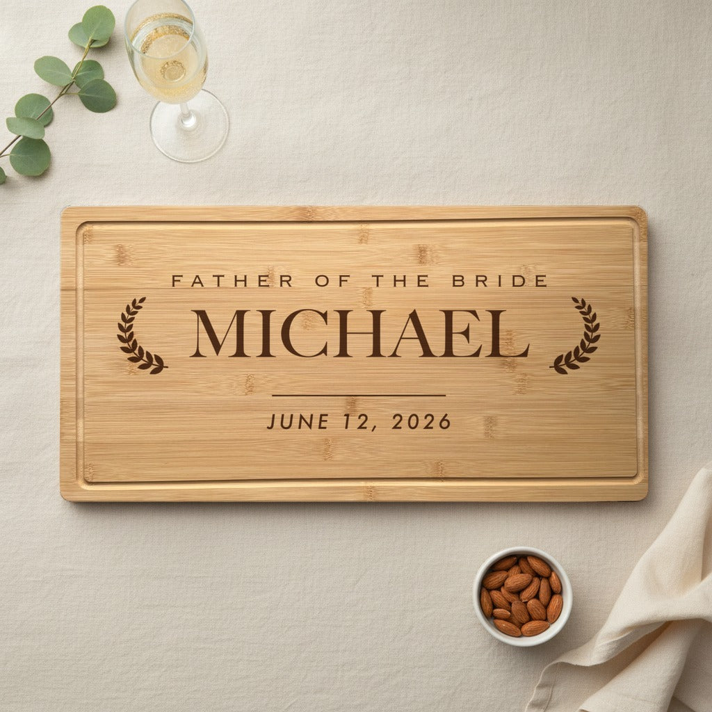 Engraved father of the bride bamboo cutting board laid on an ivory linen table with a champagne glass, eucalyptus sprig and a small dish of almonds beside it.