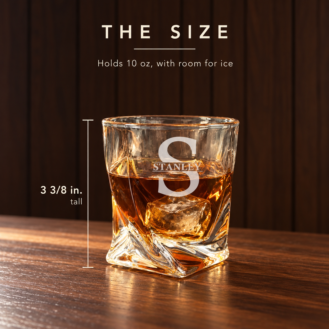 Twisted whiskey glass engraved with a large S and STANLEY, filled with bourbon and ice on a wood bar, measured 3 3/8 inches tall and holding 10 oz