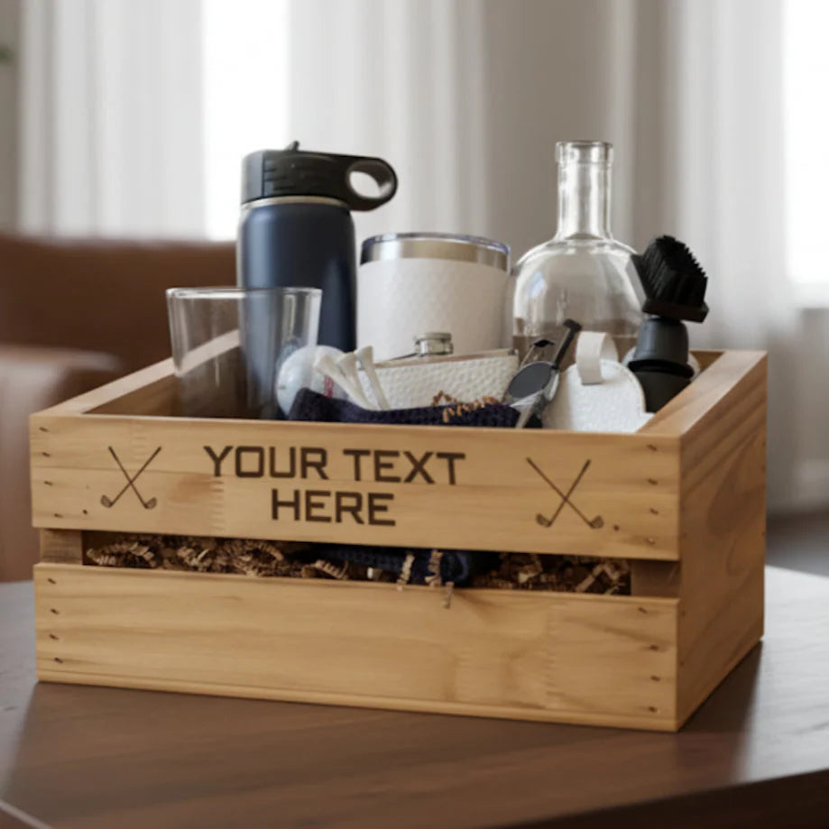 Natural wood crate with sample engraving "YOUR TEXT HERE" and crossed golf club motifs, filled with assorted golf accessories including tumbler, decanter, and towels