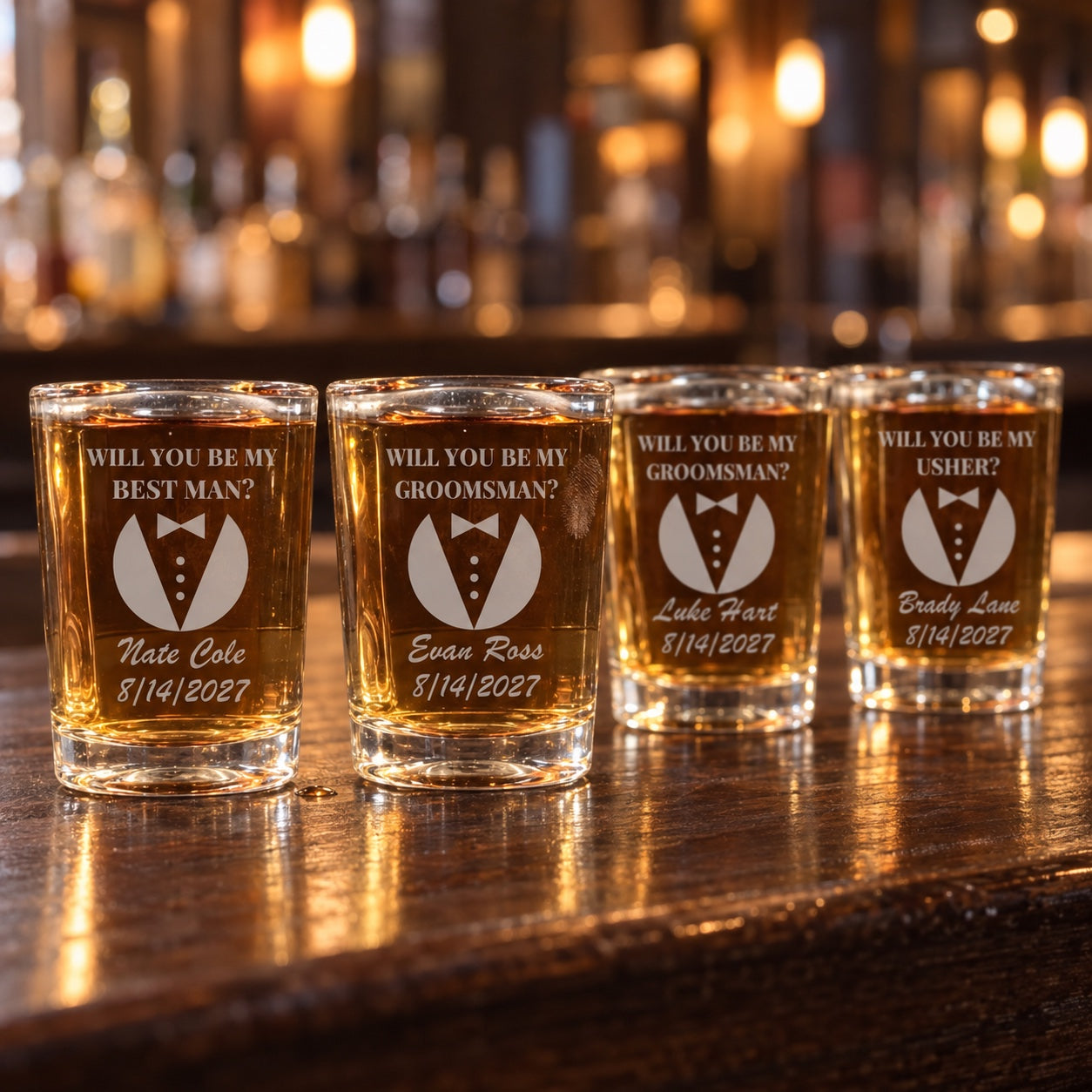 Four groomsman proposal shot glasses on a bar asking will you be my best man, groomsman or usher, each with a different name in script and a 2027 date