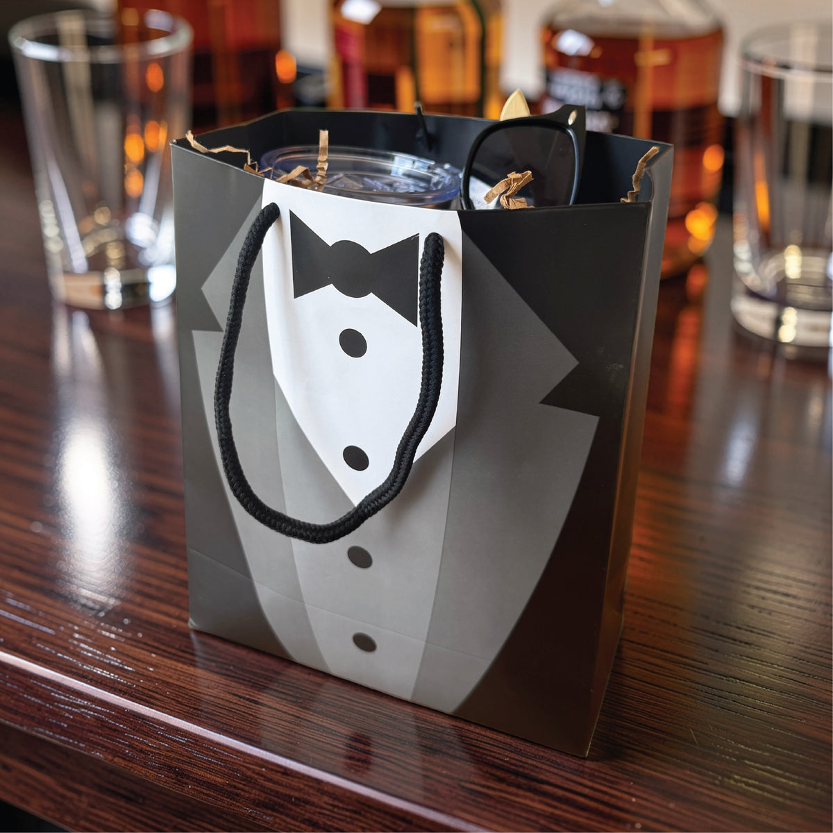 Tuxedo gift bag packed with the caricature tumbler and sunglasses, a ready to give groomsmen gift on a bar top
