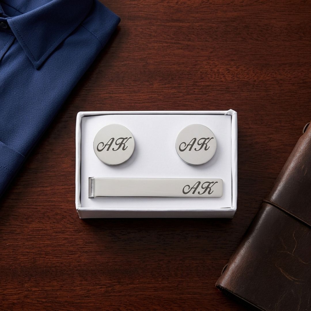Three-piece cufflink and tie bar set with monogrammed sample initials "AK" engraved on round cufflinks and rectangular bar, presented in white gift box packaging.