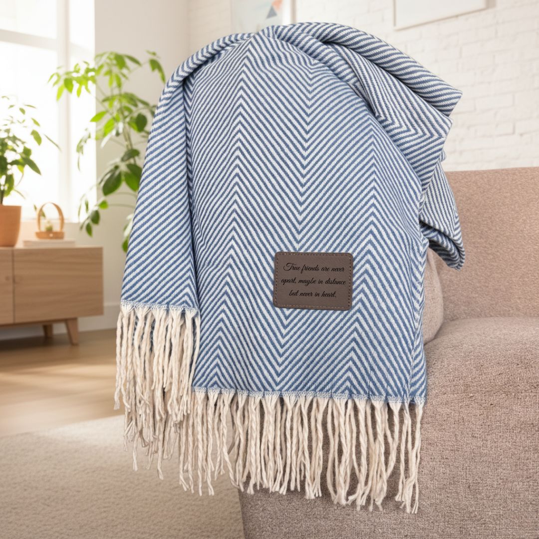 Blue and cream chevron patterned throw blanket draped over chair back, featuring fringe trim and a customizable leather patch with sample engraved text.