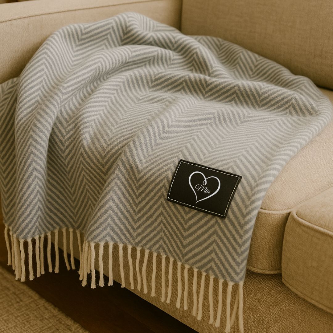 Grey and cream herringbone throw blanket with fringe trim, featuring sample personalization on black patch label with heart design and "Mia" engraving