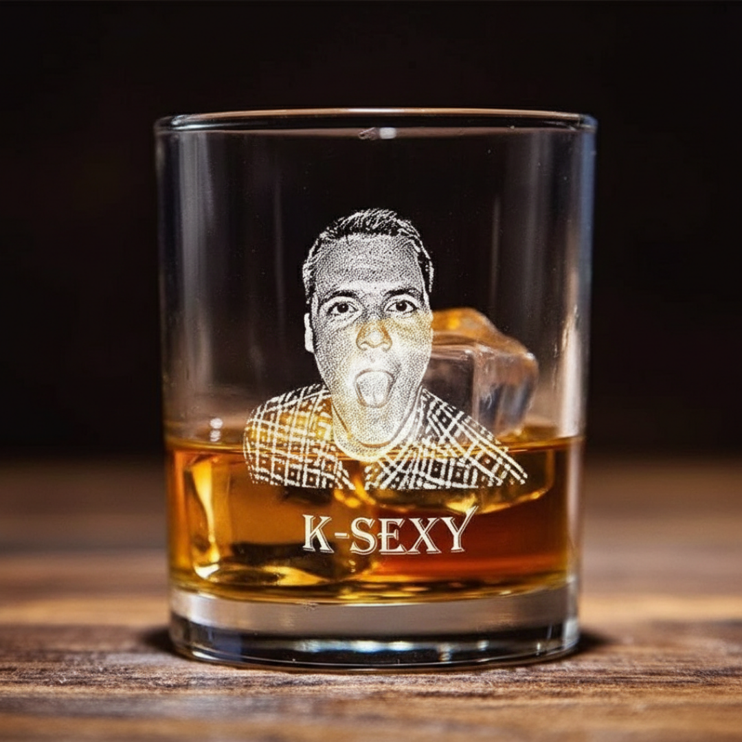 Whiskey glass filled with amber liquid, laser-engraved with sample portrait of a man's face with tongue out and text "K-SEXY" below