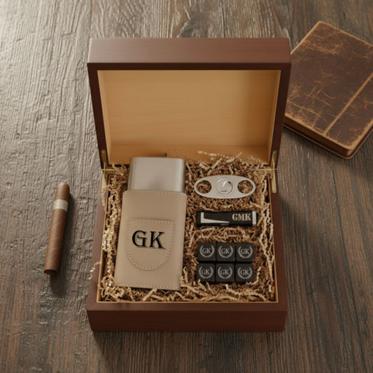 Brown wooden gift box opened to reveal cream leather cigar case engraved with sample initials "GK", personalized whiskey stones marked "GMK", silver bottle opener, and tan packing material, with cigar and leather journal beside the box.