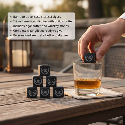 Hand placing engraved whiskey stone into glass of amber liquid, with pyramid stack of personalized stones and lantern visible on outdoor wooden table