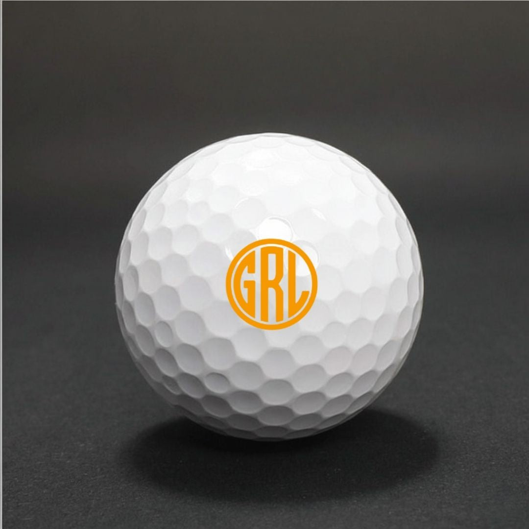 White golf ball with dimpled surface featuring sample monogram "GRL" printed in orange circular design