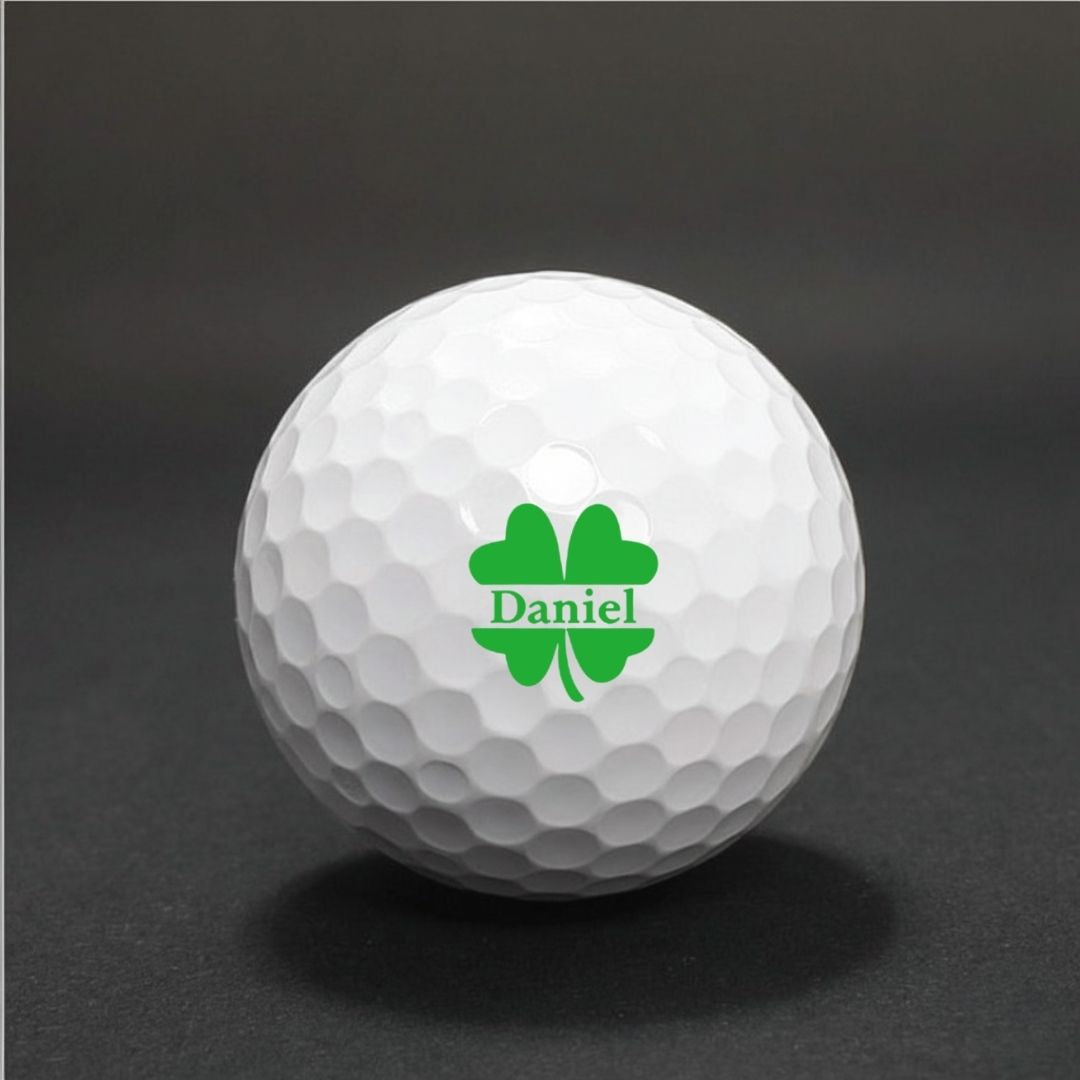 White golf ball with dimpled surface displaying sample personalization: green four-leaf clover design with name "Daniel" printed in center