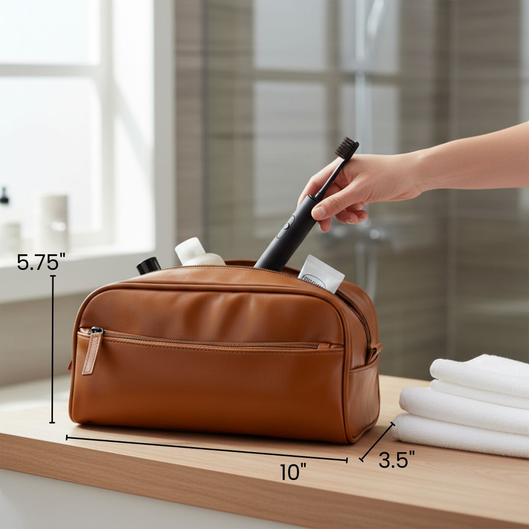 Brown leather toiletry bag displayed on wooden surface with dimensions labeled 10" x 5.75" x 3.5", featuring front zip pocket and interior compartments