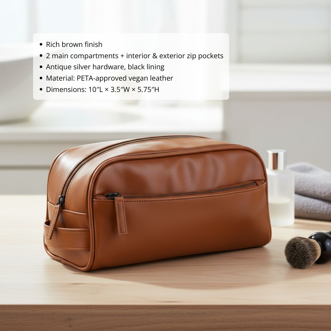 Rich brown vegan leather toiletry bag with antique silver hardware and exterior zip pocket, displayed on wooden surface next to grooming brush and skincare products