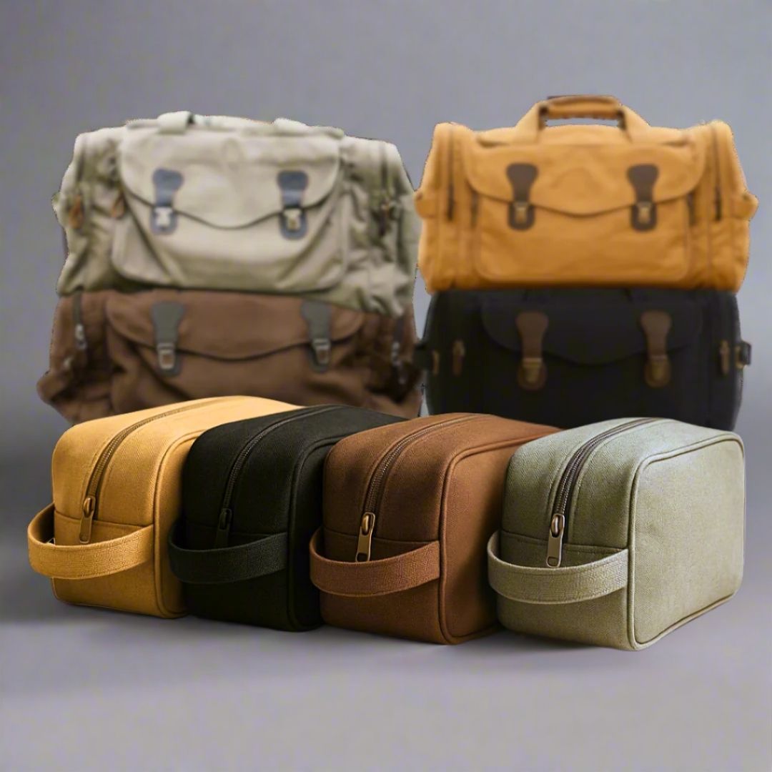Four canvas toiletry bags displayed in yellow, black, brown, and tan, with two larger duffles shown in background featuring dual handles and metal clasp closures
