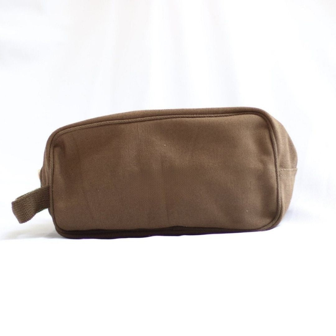 Tan canvas toiletry bag with webbing handle and flat bottom, displayed against white background