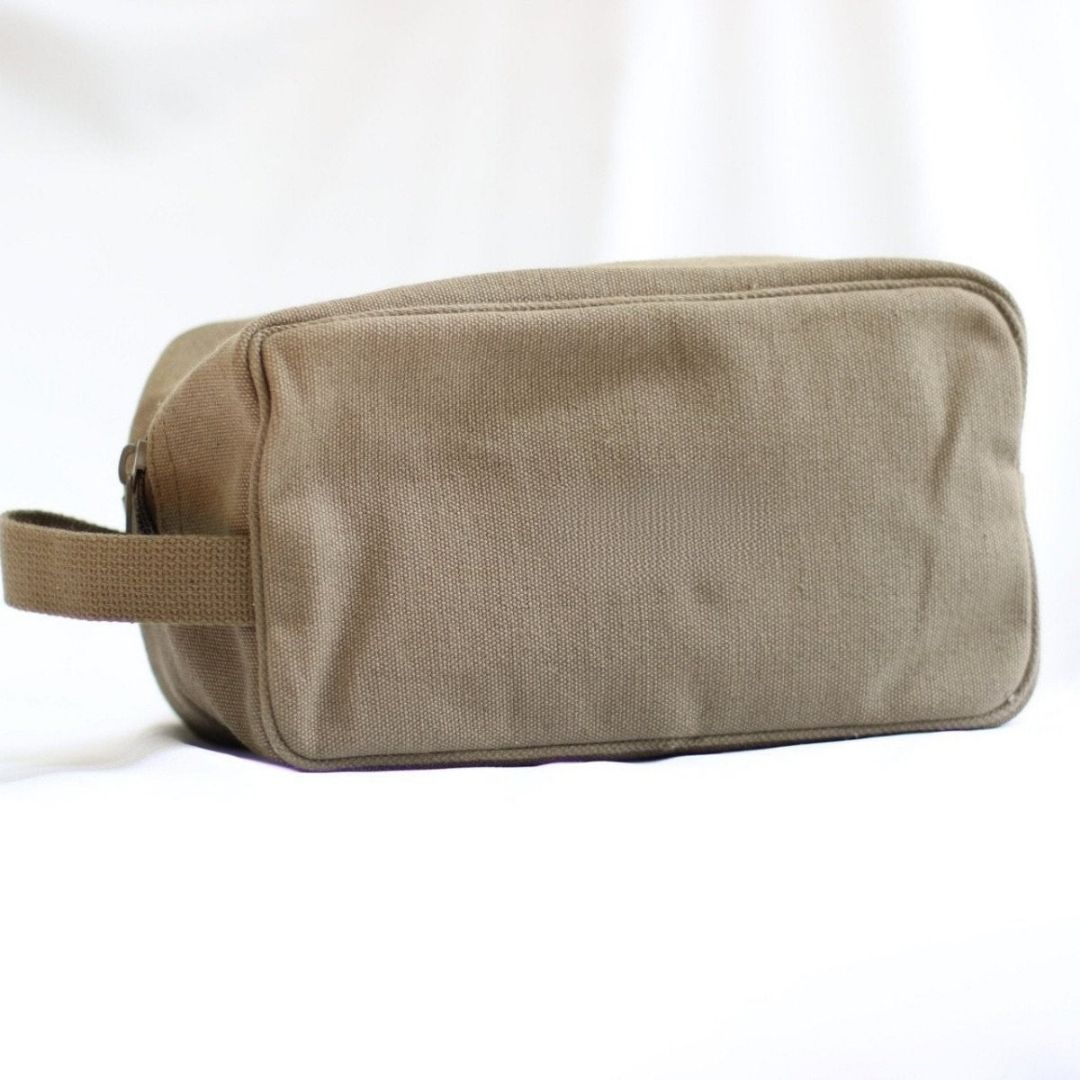 Tan canvas toiletry bag with handle, displayed at angle showing boxy rectangular shape and flat base