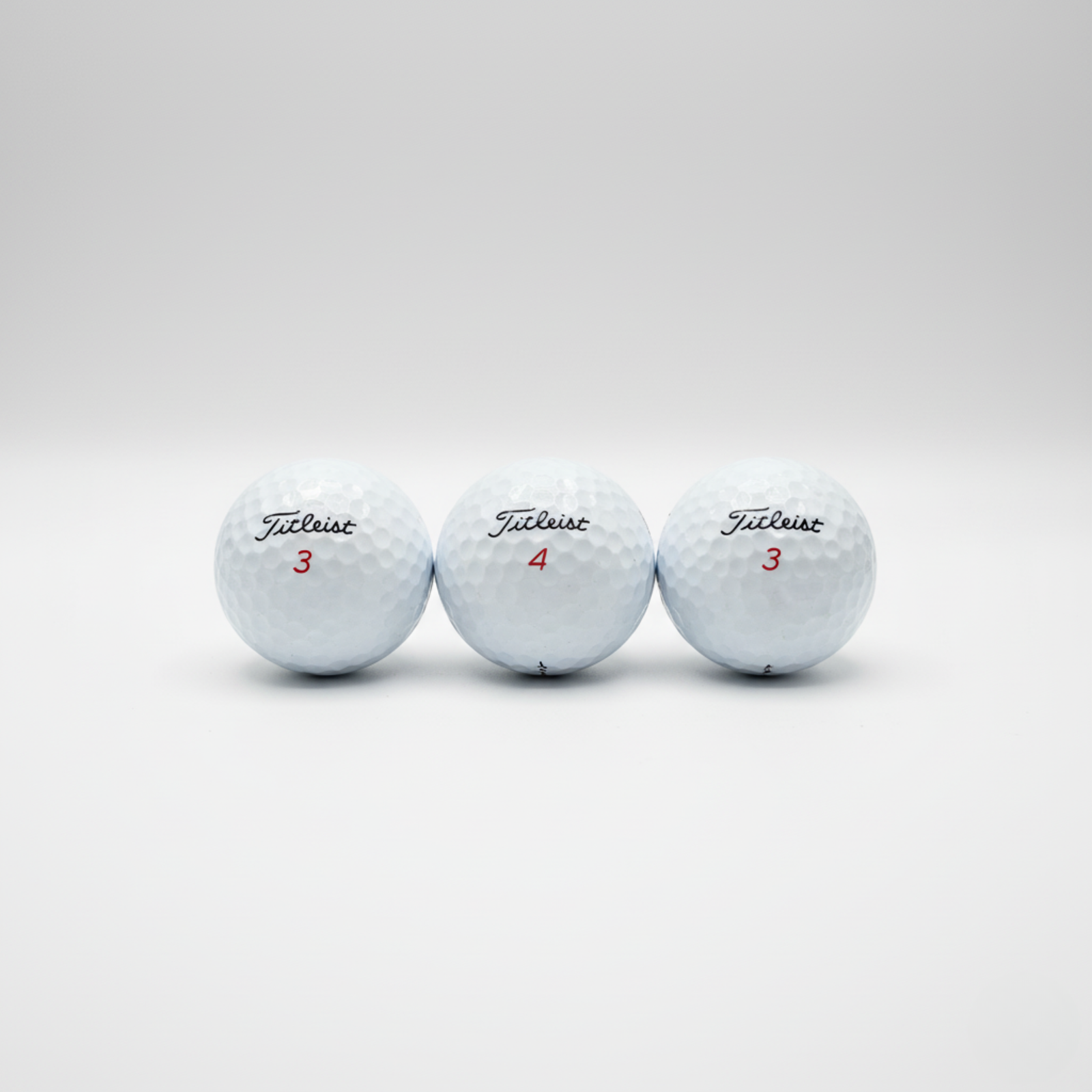 Three white Titleist golf balls with sample personalization showing red numbers 3, 4, and 3 on dimpled surface