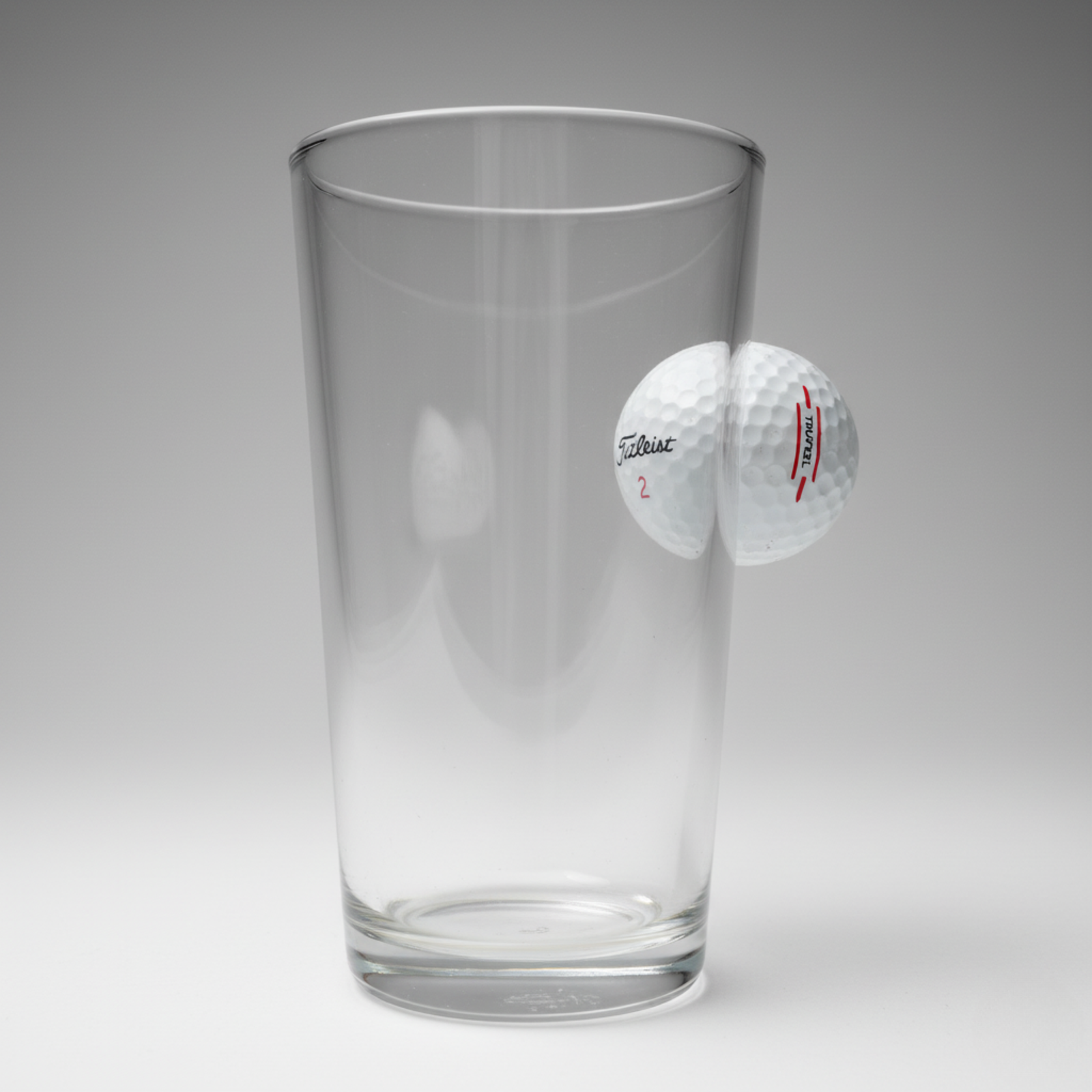 Clear glass tumbler beside a white golf ball printed with "Titleist" logo and red "Turbo" text on numbered panel