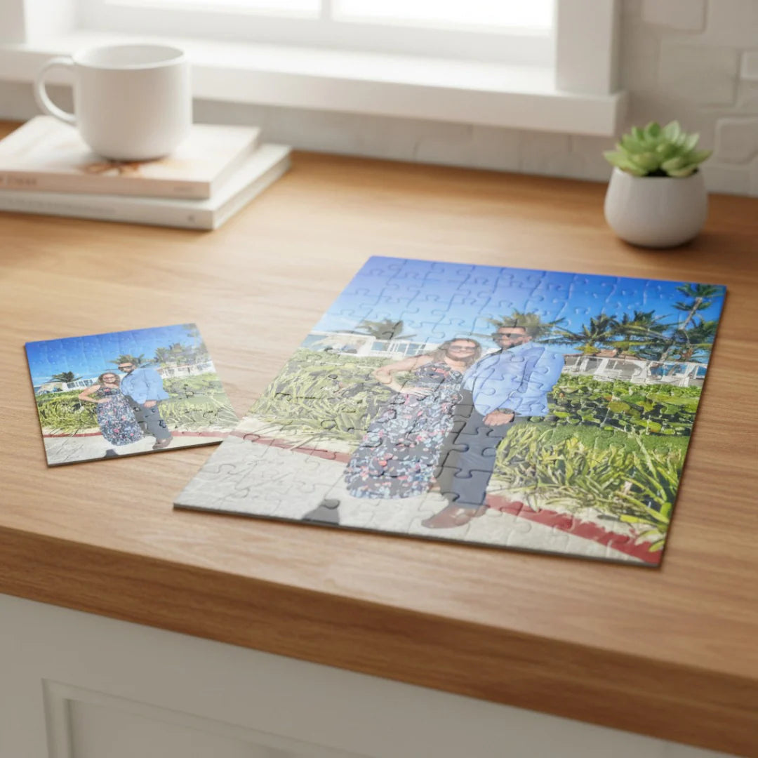Custom photo puzzle displayed partially assembled on wooden desk, showing outdoor garden scene with two people, accompanied by smaller reference photo and white mug.