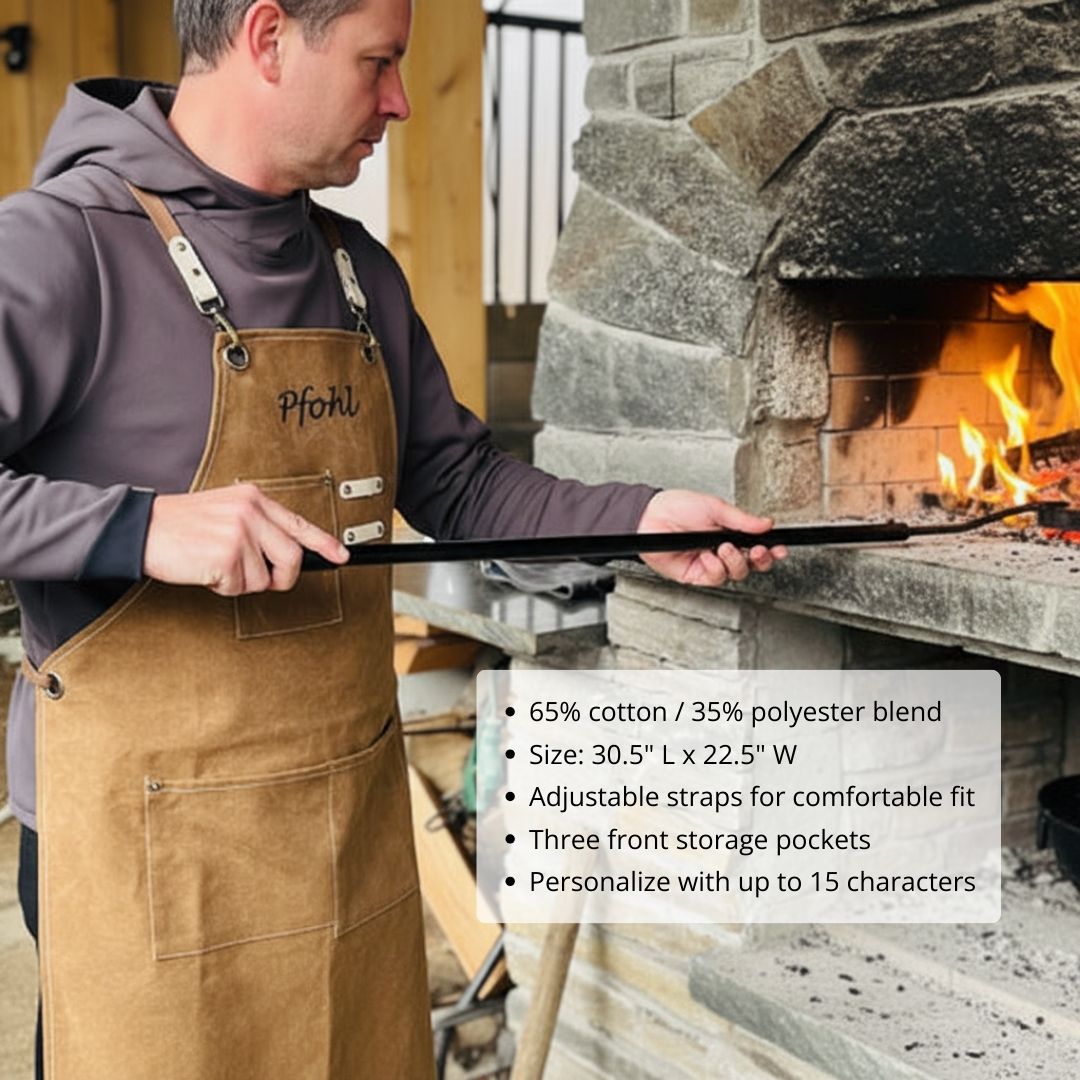 Tan canvas apron with sample personalization "pfohl" engraved on chest, worn while tending fireplace with adjustable straps and front storage pockets visible