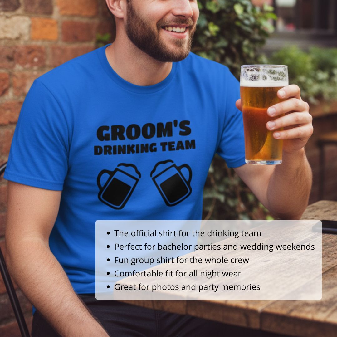 Man wearing bright blue t-shirt printed with "GROOM'S DRINKING TEAM" text and beer mug graphics, holding a glass of beer outdoors against brick wall.