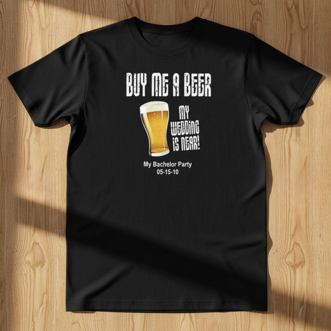 Black t-shirt with printed design reading "BUY ME A BEER MY WEDDING IS HERE" with beer glass graphic and sample text "My Bachelor Party 05-15-10