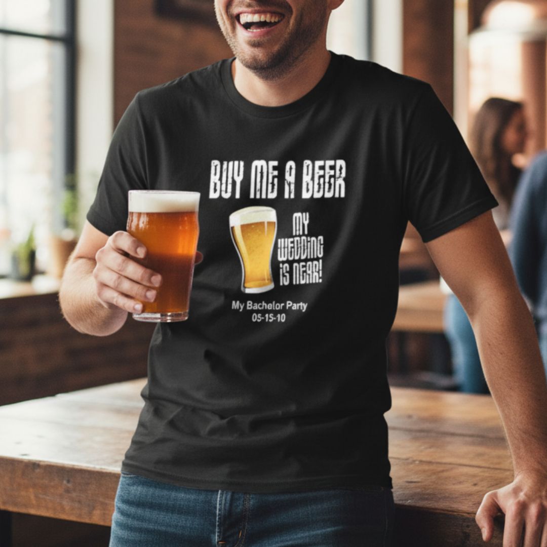 Black t-shirt with personalized "Buy Me a Beer" design, beer glass graphics, and sample text "My Bachelor Party 05-15-10" worn by man holding beer glass