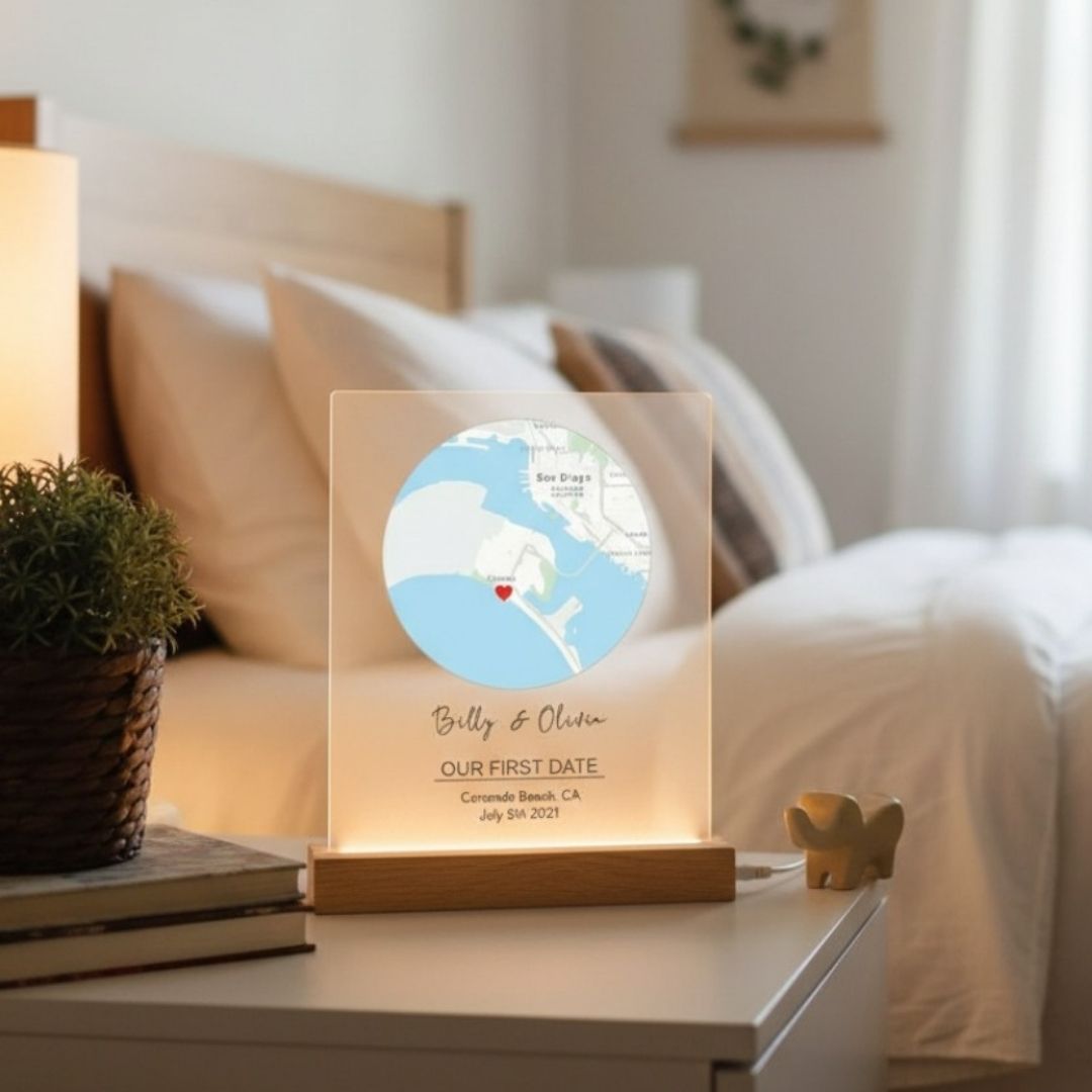 Acrylic map sign with wood base featuring sample personalization "Billy &amp; Oliver" and "OUR FIRST DATE Coronado Beach CA July 5th 2021" with heart marker displayed on bedroom nightstand