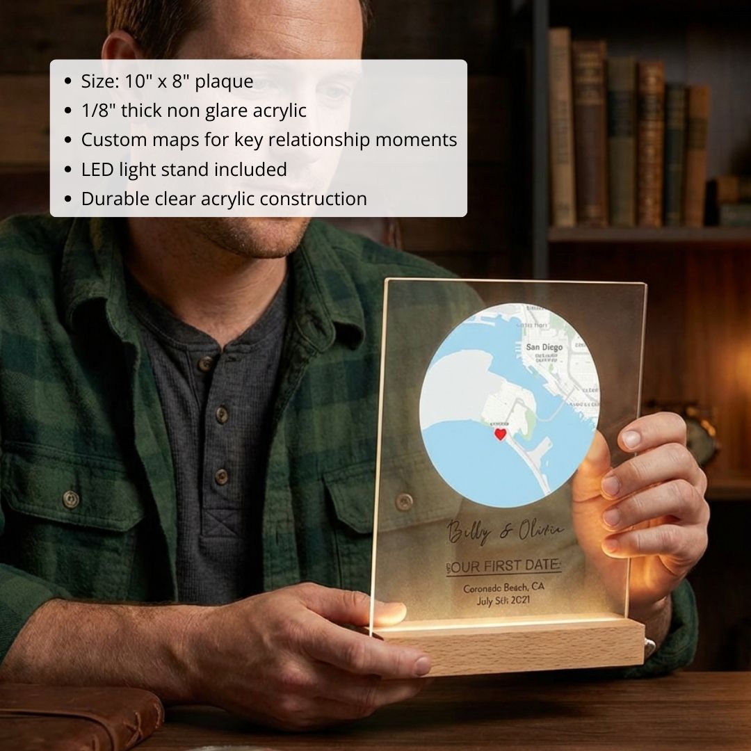 Clear acrylic map plaque with sample personalization showing "Billy & Olivia," heart marker on coastal map, and "OUR FIRST DATE" text with wooden base and LED light stand.