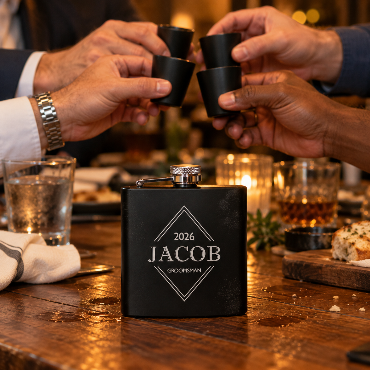 Groomsmen clink matte black shot glasses at a rehearsal dinner behind the Sharp Shooters flask engraved 2026, JACOB and GROOMSMAN on the table