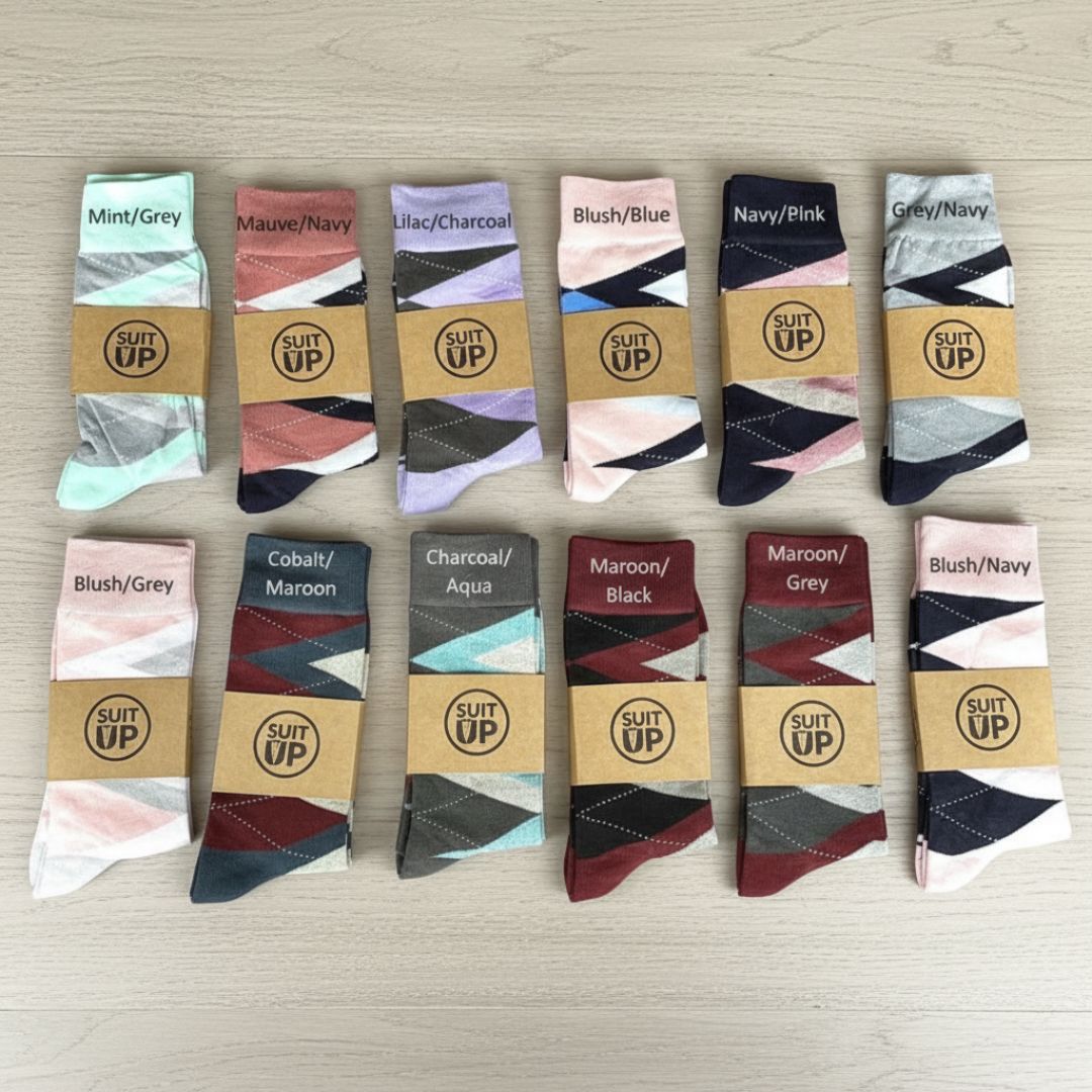 Grid display of twelve argyle patterned socks in various color combinations including mint/grey, mauve/navy, lilac/charcoal, blush/blue, navy/pink, and maroon/black options, each wrapped with kraft paper band featuring SUIT UP logo